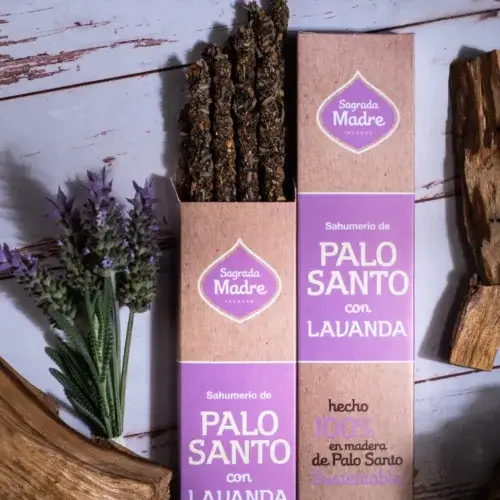 un manojo de varillas de incienso artesanal de palo santo con lavanda, mostradas en la mitad saliendo de su caja original. Rodeada de palo santo y flores de lavanda